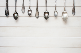 The image shows a row of metal spoons across the top of the frame on a table. The background is a light grey colour.