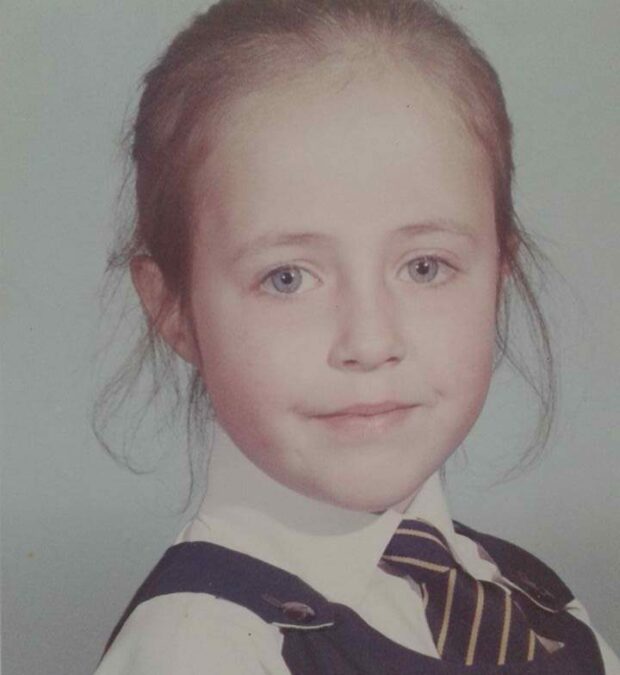 Picture of Helen as a child. Helen has light brown hair in a ponytail, wearing a blue pinny and striped tie