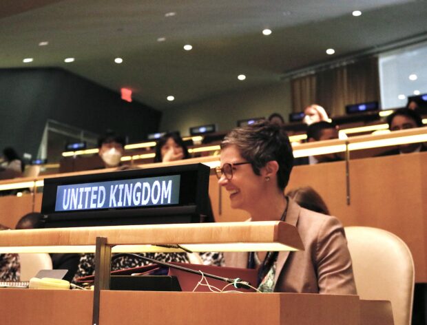 Picture of Minister for Disabled People Chloe Smith sitting at UN style wooden desk with sign saying 'United Kingdom' in front of her . Chloe is smiling and laughing