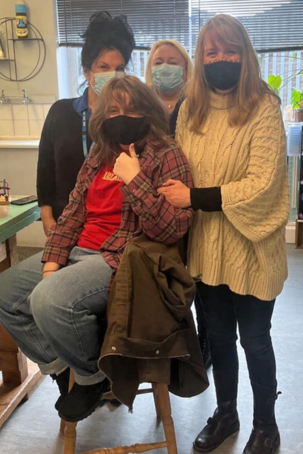 An image of four women at a vaccination centre. Three women stand around Harry's sister who is seated on a chair. All four women are wearing masks. Harry's sister Lily sat giving a thumbs-up to the camera.