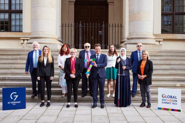 Delegation members and invited guests stand on steps next to G7 Inclusion Summit 2022 signs.