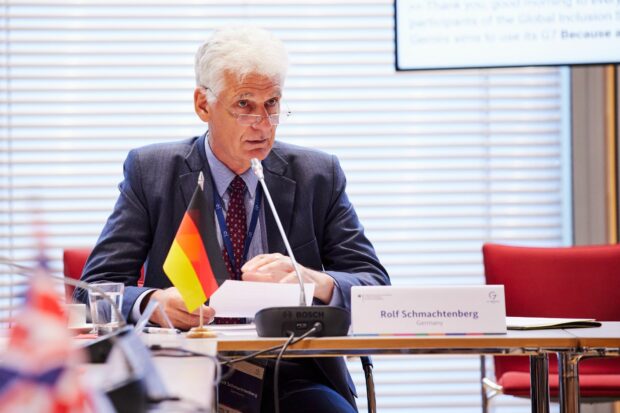 Minister Schmachtenberg speaking into his microphone, with a small German flag to his right.